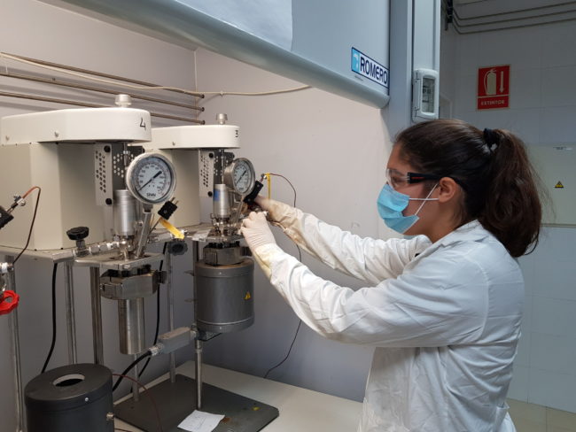 Hace poco más de un año que se lleva desarrollando una tesis doctoral, con mención Industrial, entre la Universidad de Huelva y Cepsa, encaminada al desarrollo de nuevas estrategias para la conversión directa de benceno en fenol. El fenol es producto fabricado en la Planta Química de Palos que se usa, principalmente, en la producción de resinas y agroquímicos; manufactura de nylon y otras fibras sintéticas; industria farmacéutica y clínica como un potente fungicida, bactericida, antiséptico y desinfectante; bisfenol A (materia prima para producir resinas epoxi y policarbonatos) y en el proceso de fabricación de ácido acetilsalicílico (aspirina), entre otras aplicaciones. El proceso actual de producción de fenol en la planta química de Cepsa en Palos parte de benceno y consta de muchas fases consecutivas hasta llegar a la molécula de fenol. Sustituir este proceso por otro de una sola fase supondría, no solo un hito tecnológico de carácter mundial, sino un considerable ahorro energético y una contribución notable a la sostenibilidad del proceso. La tesis industrial desarrollada en la Universidad de Huelva y codirigida por personal de Cepsa explora un método novedoso para pasar directamente de benceno a fenol mediante catalizadores que trabajan en medios no habituales. Los directores de la tesis son los profesores Ana Caballero y Pedro J. Pérez, del Laboratorio de Catálisis Homogénea (LCH) del Centro de Investigación en Química Sostenible (CIQSO), y Jesús Lázaro, coordinador del Departamento de Petroquímica y Nuevos Materiales del Centro de Investigación de Cepsa. La investigadora en dicho proyecto es la doctoranda Elena Borrego Blanco, Graduada en Química por la Universidad de Sevilla y Máster en Química por la Universidad de Barcelona. En este primer año, del total de tres de los que constará el periodo doctoral, ya se han producido los primeros resultados que permiten augurar el éxito del programa de trabajo inicialmente establecido. En esta modalidad de tesis doctoral industrial, uno de los requisitos es la contratación directa de la doctoranda por parte de Cepsa, empresa promotora de la investigación; por su parte, la Universidad de Huelva cofinancia con la compañía energética los costes salariales dentro de su Estrategia de Política de Investigación y Transferencia. Adicionalmente, los trabajos experimentales cuentan con el apoyo económico de la Catedra Fundación Cepsa que cubre los gastos de materiales y reactivos derivados de estas investigaciones a través del Convenio de Colaboración que cada año suscribe con la Onubense. La dilatada experiencia de los investigadores del CIQSO, unida a la experiencia del Centro de Investigación de Cepsa en el campo de la oxidación de compuestos aromáticos, se han unido para abordar este complejo tema en el que se espera lograr un avance, no solo en el conocimiento científico, sino en la posible aplicación industrial de los conocimientos generados. El LCH es uno de los grupos de investigación con mayor actividad, en lo que a resultados de investigación se refiere, de la Universidad de Huelva. Desarrolla proyectos de investigación de diversa naturaleza, financiados a partir de convocatorias públicas competitivas a nivel estatal o autonómico, así como por diversas empresas del ámbito químico. Su actividad ha sido reconocida a través de diversos premios y distinciones internacionales y nacionales. En sus 24 años de historia este grupo, que fue fundado en 1996 por el profesor Pérez, ha dado luz a 20 Tesis Doctorales ya defendidas, y otras seis que se encuentran actualmente en fase de desarrollo, entre las que se incluye esta de carácter industrial. Desde la Universidad de Huelva se ha subrayado que la alianza con Cepsa permite la constante transferencia del conocimiento, uno de los valores más importantes de la UHU, y es un instrumento esencial para el desarrollo de la investigación y la formación y empleabilidad de los estudiantes. Las cátedras de la Fundación Cepsa Las cátedras de la Fundación Cepsa en las Universidades de Huelva, Cádiz, Sevilla, La Laguna y Politécnica de Madrid, se refuerzan continuamente gracias a las aportaciones y a la implicación de los profesionales de la Compañía y de las instituciones académicas comprometidas, en la mejora de investigación, la formación, flujo de conocimiento y la innovación. Las Cátedras Fundación Cepsa han permitido a miles de alumnos acercarse al mundo laboral y aproximar a los profesores universitarios a la realidad de los sectores energético y químico. El intercambio de conocimientos y experiencia entre los profesionales de Cepsa y docentes y alumnos universitarios supone, desde hace dos décadas, el enriquecimiento profesional de todos ellos. Por todo ello, Cepsa es una gran aliada de estas universidades.