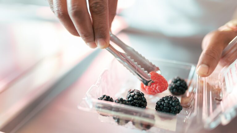 An ice-cream parlor worker is preparing some raspberry and blackberries on the roll machine using tongs