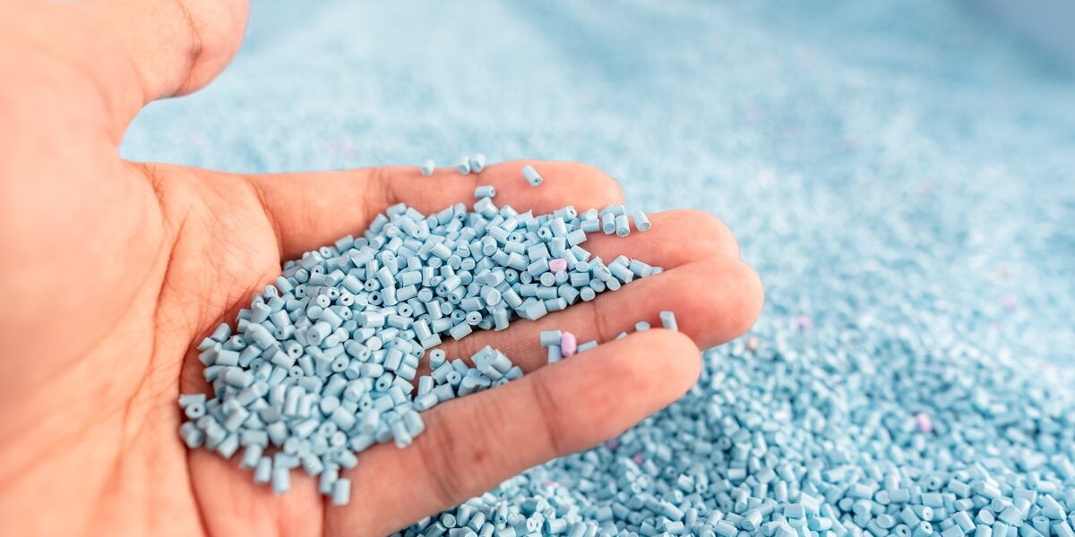 Hand on large pile of blue plastic granules in temporary storage
