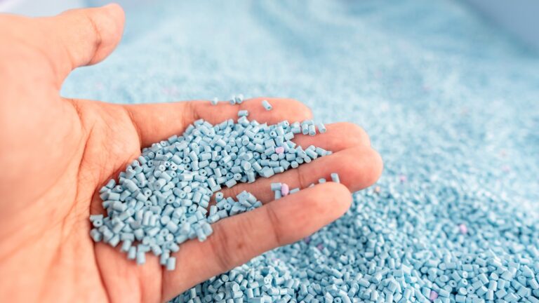 Hand on large pile of blue plastic granules in temporary storage