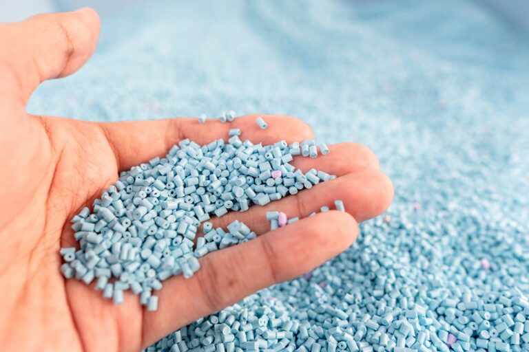 Hand on large pile of blue plastic granules in temporary storage